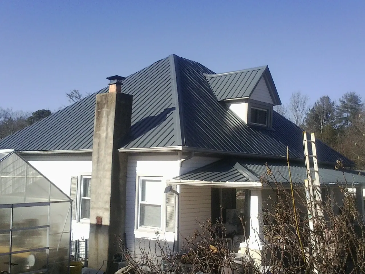 Dark blue standing seam metal roof on a white farmhouse with dormer — Slate & Tile Roof Repair by Roofing Brothers in Goode