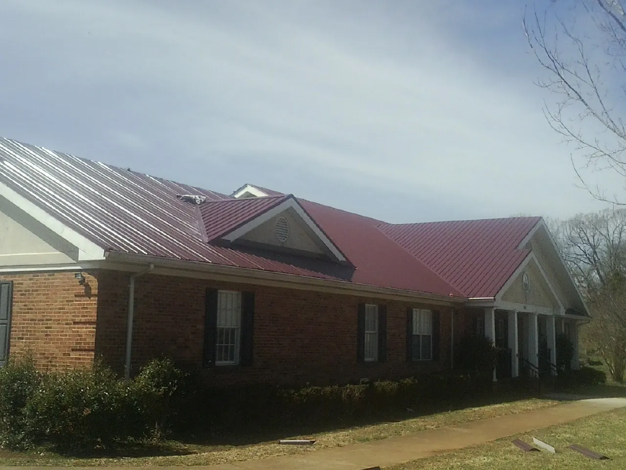Red metal roof with gabled entries on a long brick building, from a Hail Damage Roof Repair job in Goode