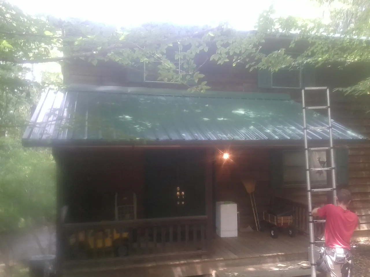 Worker on a ladder at the green porch roof of a wooded cabin in Goode